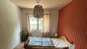 Une chambre à coucher avec un lit en bois, une table de chevet, un luminaire suspendu, une fenêtre avec des rideaux et une plante en pot.
