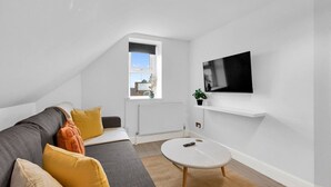 Una sala de estar moderna con un sofá gris, una mesita blanca y un televisor montado.
