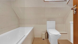 Un baño con bañera, inodoro y ventana sobre el inodoro.