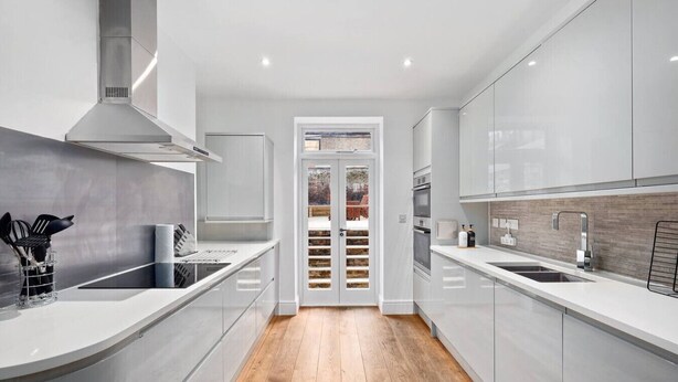 Une cuisine moderne avec des meubles blancs, une hotte en acier inoxydable et un plancher en bois.