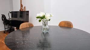 Une table ronde ornée d’un vase de fleurs blanches, une chaise noire et un piano en arrière-plan.
