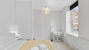 Ein modernes Schlafzimmer mit Bett, Nachttisch, Schreibtisch, Stuhl und einem großen Fenster.