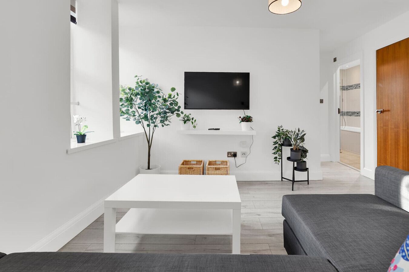 A modern living room with a white coffee table, grey sofa, and a TV mounted on the wall.
