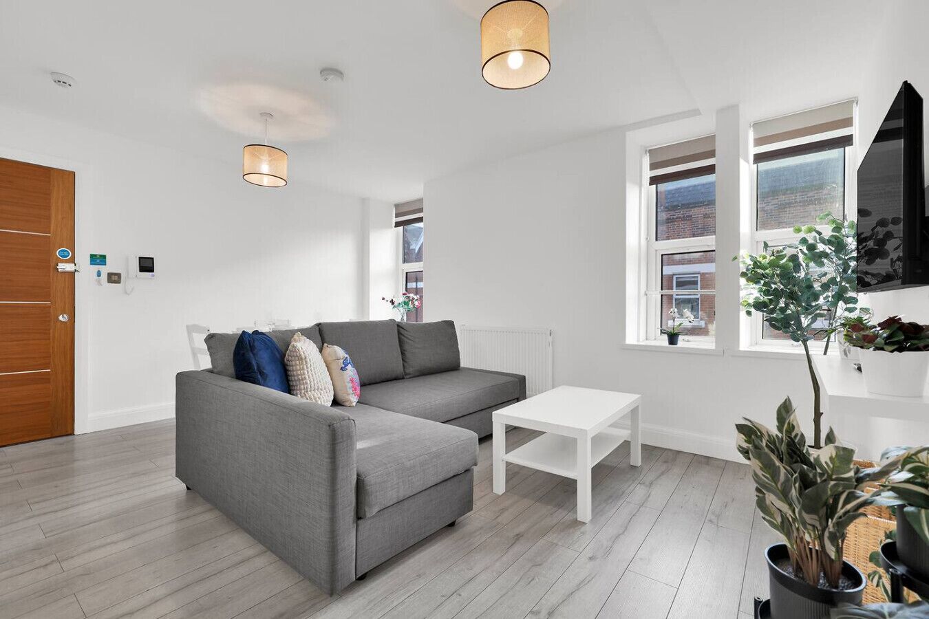 A modern living room with a grey sofa, white coffee table, and potted plants.