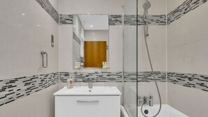 Ein modernes Badezimmer mit einer gläsernen Duschkabine, einem weißen Waschbecken und einem Spiegel darüber.