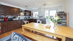 A modern kitchen with wooden cabinets, a dining table, and a built-in washing machine. - Cosy Clapham Retreat - 2 Min Walk To Tube (Greater London)