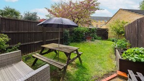 Un jardin avec une table et un banc en bois, un parasol pour pique-nique et un parterre fleuri.