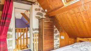 Een slaapkamer met een schuine plafond, een houten garderobe en een bed met een geborduurde spreideken.