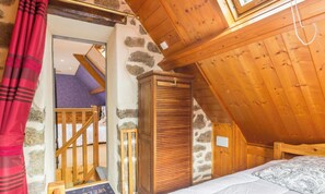 A bedroom with a sloped ceiling, wooden wardrobe, and a bed with a patterned bedspread.