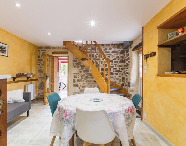 A dining area with a round table, chairs, a staircase, and stone walls. - Quaint house, pets welcome - 3 guests (Fermanville)