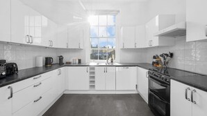 A modern kitchen with white cabinets, a black countertop, a window with a view, and a stove. - Chic 1BR Flat Walk to King’s Cross & St Pancras (Greater London)