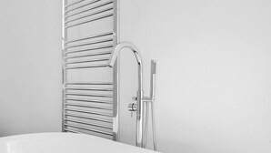A modern bathroom with a chrome bathtub, a wall-mounted towel rack, and a handheld showerhead. - Chic 1BR Flat Walk to King’s Cross & St Pancras (Greater London)