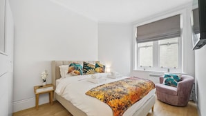 Un dormitorio con cama, mesita de noche, silla, ventana y vistas al exterior.