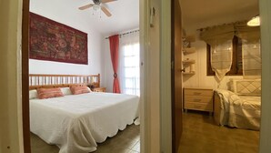 A bedroom with a bed, a ceiling fan, a tapestry, and a window with curtains. - Cozy townhouse with pool - 4 guests (Torredembarra)