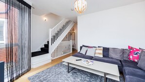 Una sala de estar moderna con una escalera, un juego de sofás, una mesa de centro y una lámpara colgante.
