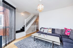 Ein modernes Wohnzimmer mit Treppe, einer Sofagarnitur, einem Couchtisch und einer Pendelleuchte.