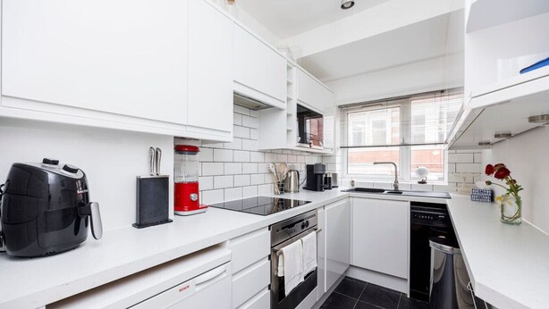 Una cocina moderna con armarios blancos, un lavavajillas Bosch, una cafetera roja y un tostador negro.