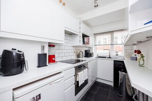 A modern kitchen with white cabinets, a Bosch dishwasher, a red coffee maker, and a black toaster. - 3BR in Covent Garden Retreat - 6 people (Greater London)