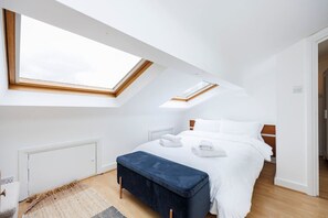 Ein modernes Schlafzimmer mit Dachfenster, einem Bett mit weißer Bettwäsche, einer blauen Bank und Holzboden.