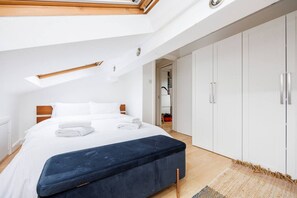 Ein modernes Schlafzimmer mit Oberlicht, einem großen Bett, einer dunkelblauen Bank und weißen Kleiderschränken.