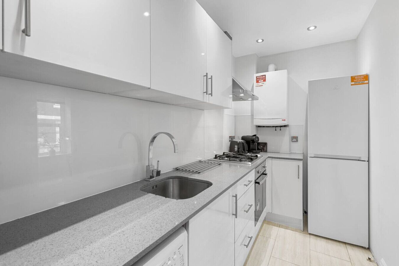 A modern kitchen with a stainless steel sink, a gas stove, a coffee maker, and a refrigerator.