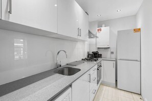 A modern kitchen with a stainless steel sink, a gas stove, a coffee maker, and a refrigerator. - Perfectly Located 2BR Apartment in Balham (Greater London)