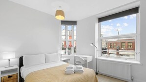 Ein modernes Hotelzimmer mit einem großen Bett, einem Schreibtisch, einem Stuhl, einem Heizkörper und einem Fenster mit Blick auf die Stadt.