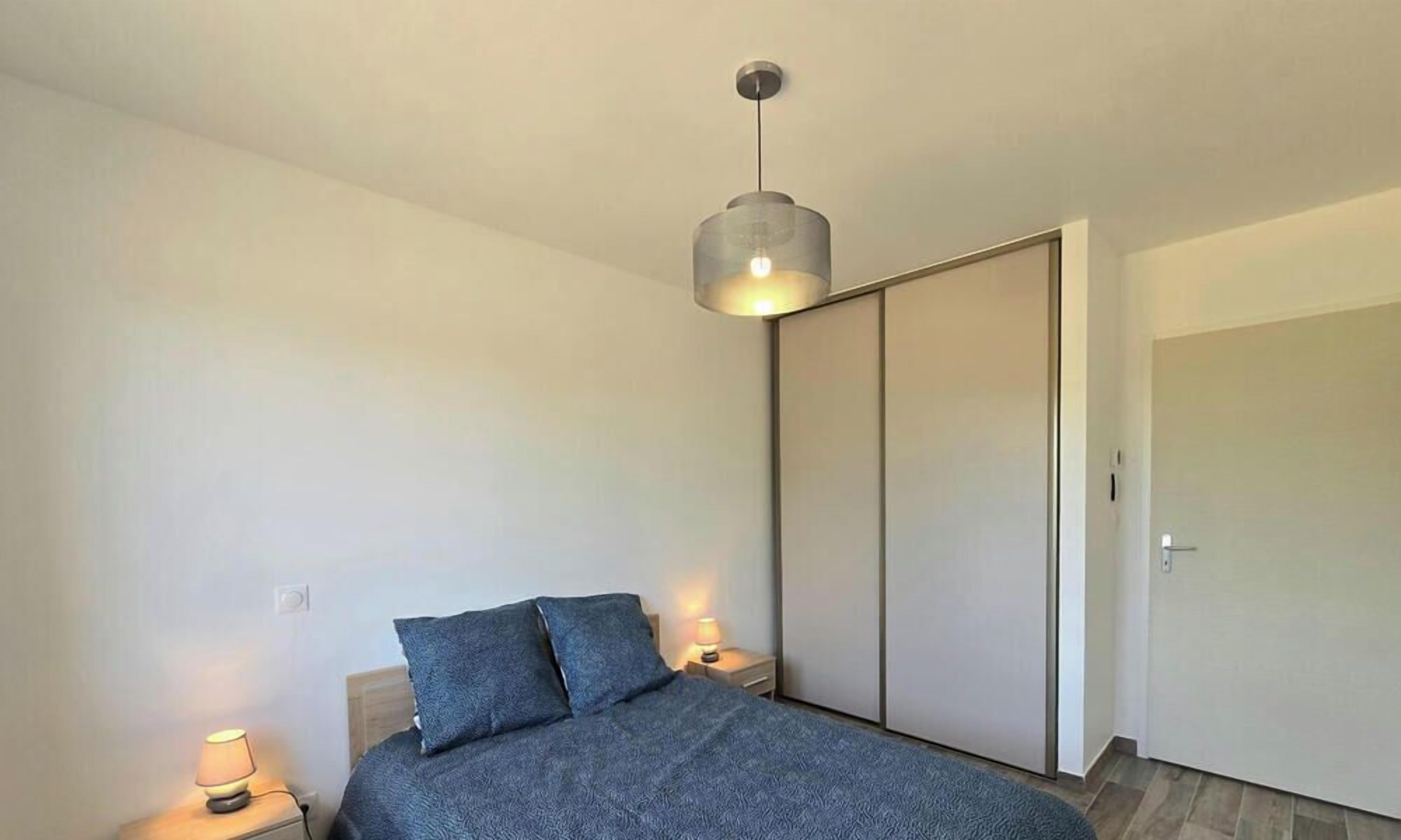 A bedroom with a bed, bedside lamps, a hanging light fixture, and a sliding door.