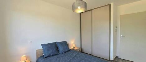 A bedroom with a bed, bedside lamps, a hanging light fixture, and a sliding door.