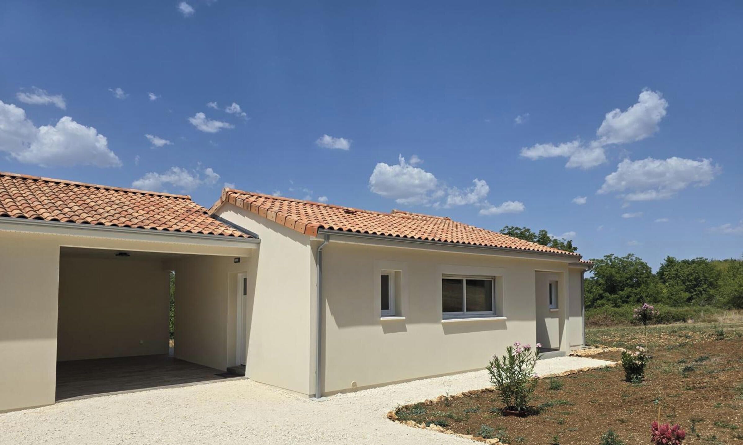 A two-story building with a tiled roof, a covered driveway, and a small garden area.