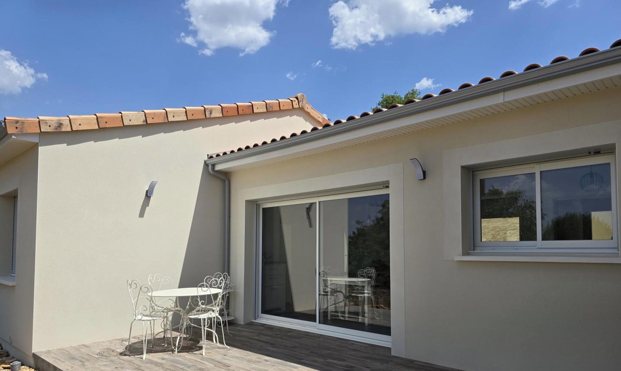 Un bâtiment moderne doté d’un toit plat, de grandes portes-fenêtres coulissantes et d’un patio aménagé avec une table et des chaises.