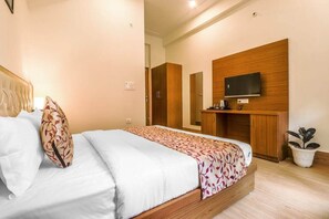 Quarto com cama, televisão na parede, mobiliário de madeira e um vaso com planta.