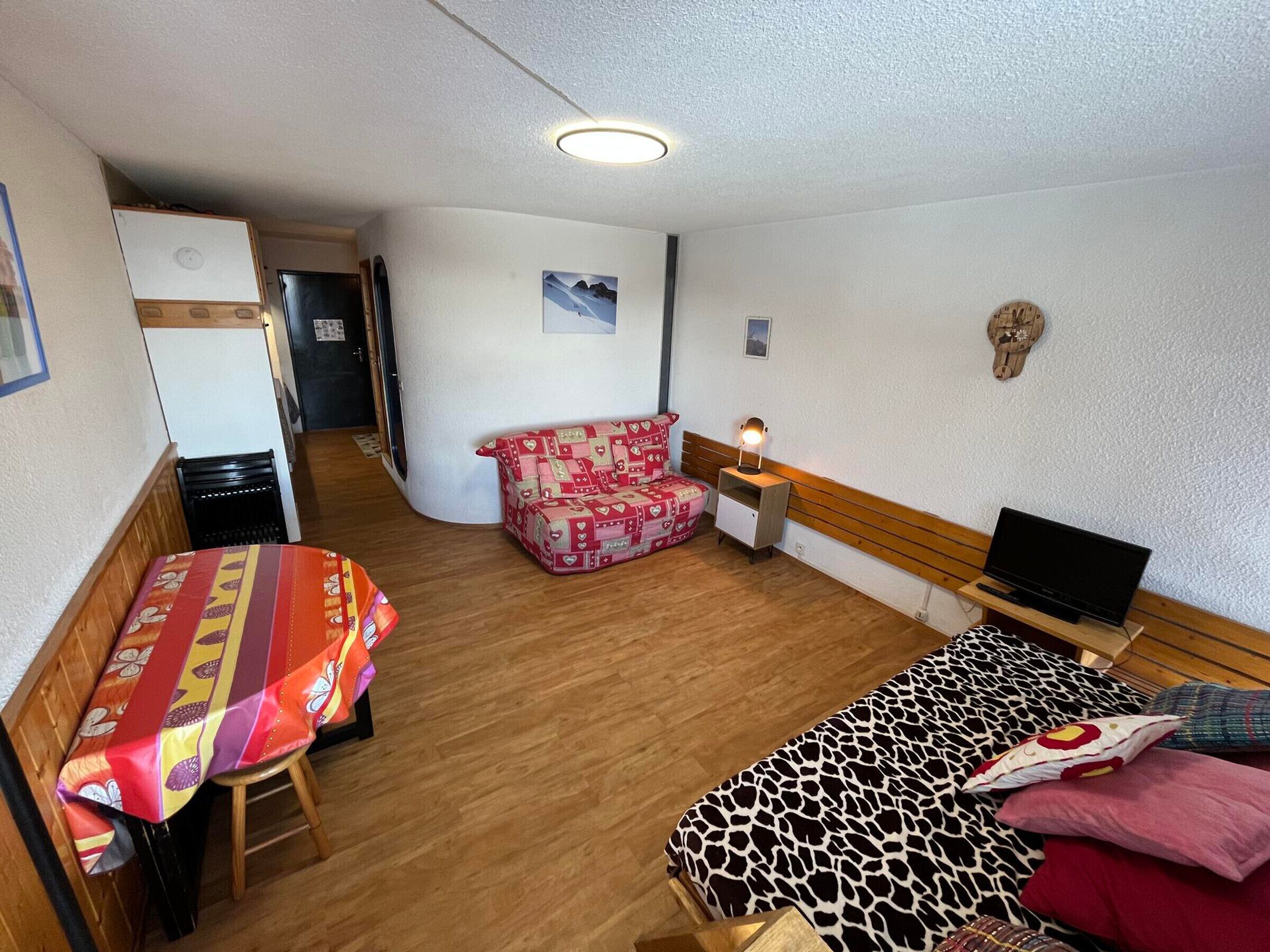 Ein kleines Zimmer mit Bett, Sofa, Tisch, Fernseher und Schreibtisch.