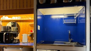 Keittiössä on sininen seinä, ruostumattomasta teräksestä valmistetut kodinkoneet, kahvinkeitin ja pesuallas.