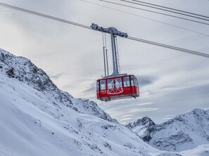 Un téléphérique rouge suspendu au-dessus d’un paysage montagneux enneigé.