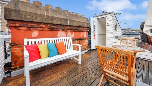 Een terras op het dak met een witte bank, een houten tafel en een bakstenen muur.