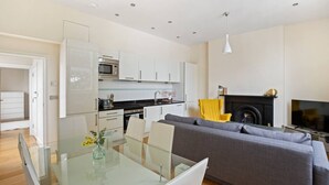 A modern kitchen with white cabinets, a microwave, and a dining area with a glass table and chairs. - 1BR Kensington | High St Kensington Tube&Hyde Park (Greater London)