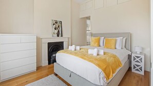 A bedroom with a bed, a fireplace, a painting, and a nightstand. - 1BR Kensington | High St Kensington Tube&Hyde Park (Greater London)