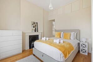 A bedroom with a bed, a fireplace, a painting, and a nightstand. - 1BR Kensington | High St Kensington Tube&Hyde Park (Greater London)