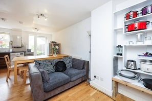 A modern kitchen with a grey sofa, wooden dining table, and white cabinetry. - Double Bedroom 2 Min To Tube (Greater London)