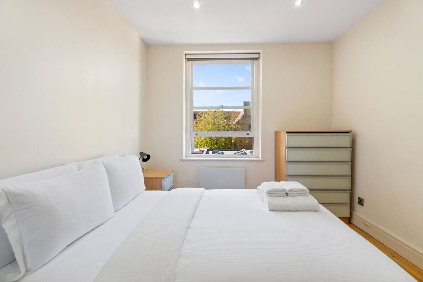 A bedroom with a bed, a nightstand, a lamp, a window, and a dresser.