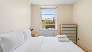 A bedroom with a bed, a nightstand, a lamp, a window, and a dresser.