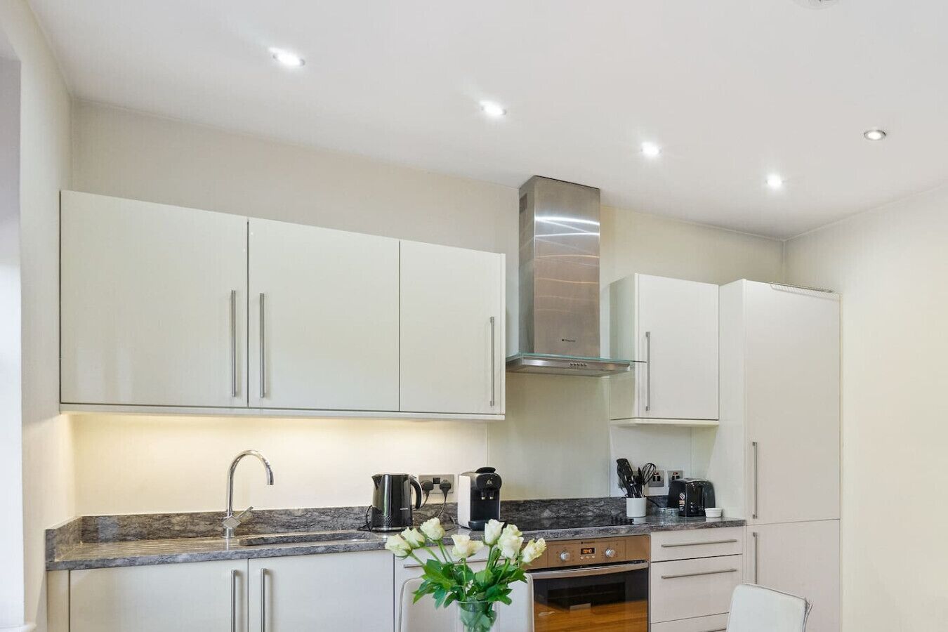A modern kitchen with white cabinets, a stainless steel range hood, and a marble countertop.