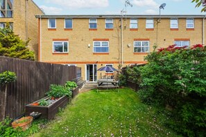 A two-story brick apartment building with a small backyard, a wooden fence, and a satellite dish. - Spacious Double Ensuite 2 Min To Tube (Greater London)