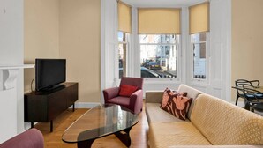 Sala de estar con televisor, sofá, sillón y una mesa de centro de vidrio.