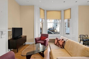 Ein Wohnzimmer mit Fernseher, Sofa, Sessel und einem Glastisch.