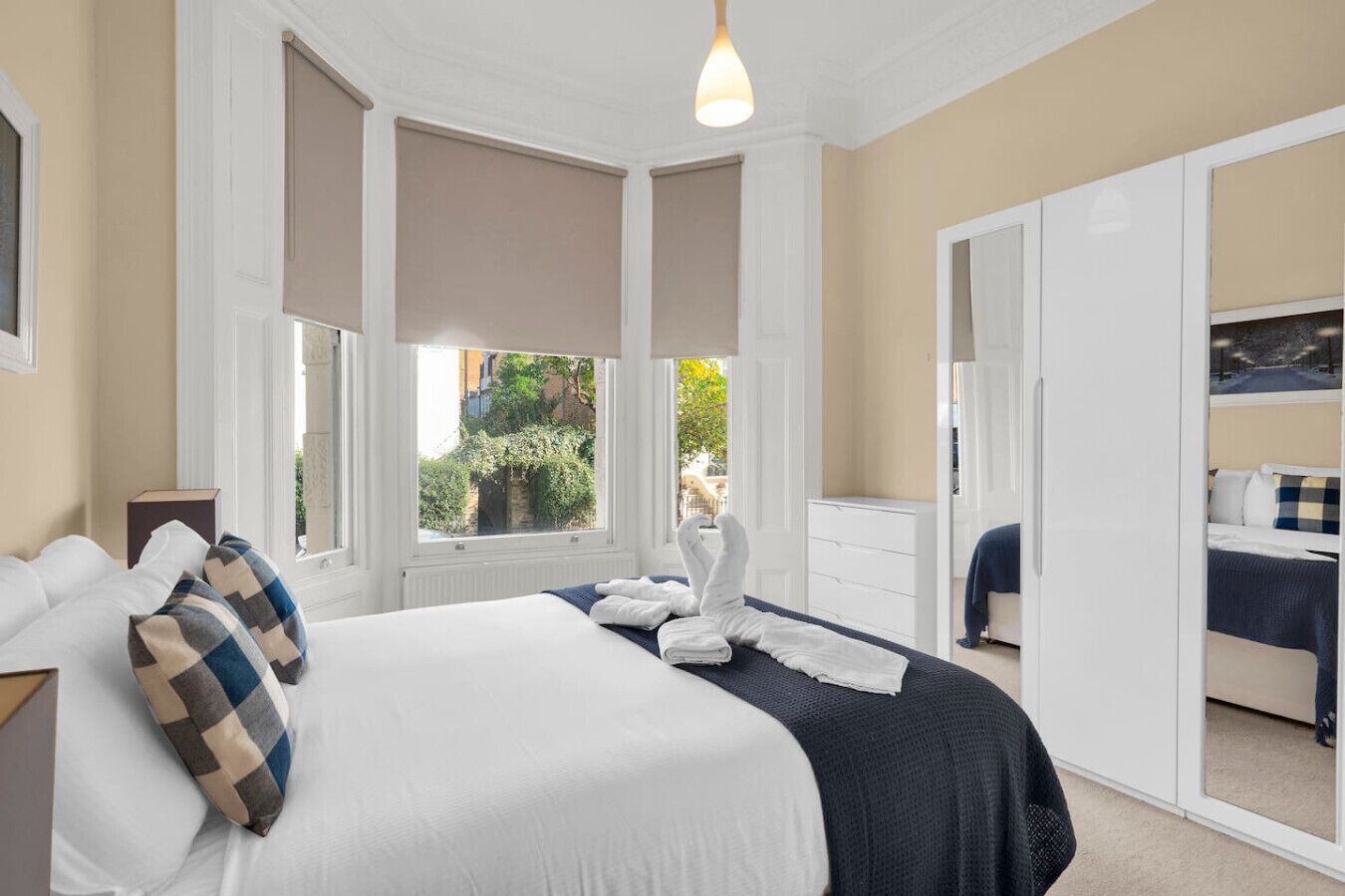 A hotel room with a large bed, a dresser, a mirror, and a view of greenery outside.