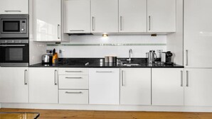 Una cocina moderna con armarios blancos, encimera negra, microondas, tostadora y cafetera.