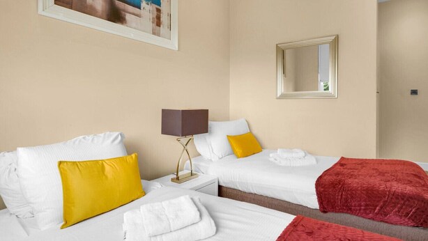 Habitación de hotel con dos camas, una mesita de noche, una lámpara y un espejo.