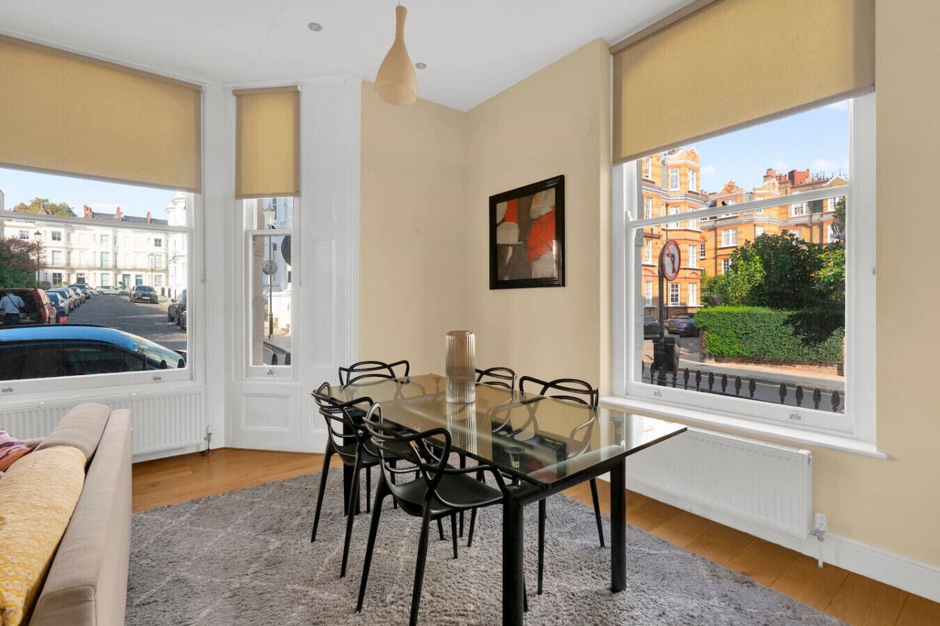 En matplats med ett glasbord och stolar, ett element, en soffa och utsikt över byggnader och parkerade bilar genom stora fönster.